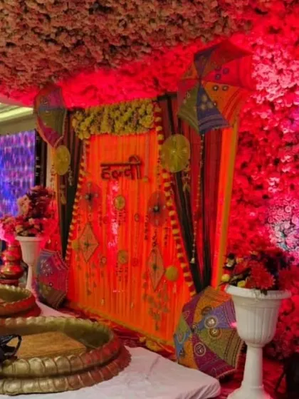 A grand Haldi decoration for a banquet hall, featuring a floral ceiling and dramatic red lighting. The setup includes traditional urlis for the ceremony, set against a richly decorated backdrop.