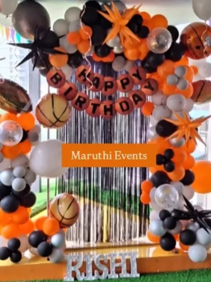 An all-sports theme party with basketball and football props. The black and orange balloon arch frames a foil curtain, creating an energetic backdrop.