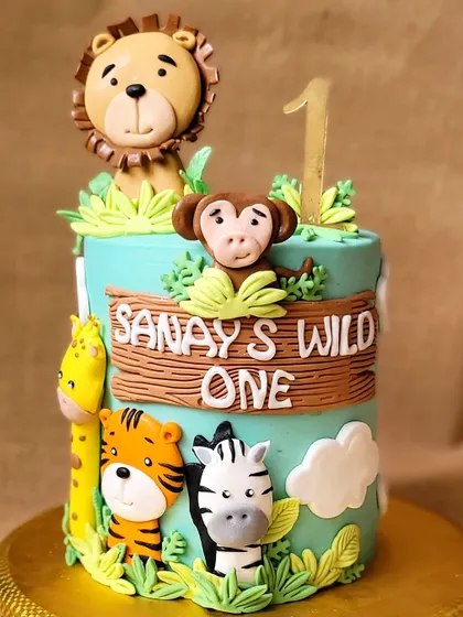A "Wild One" jungle theme cake for a first birthday. This cake is decorated with adorable, friendly fondant animals like a lion, tiger, monkey, and giraffe.