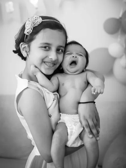 A big sister holds her yawning newborn sibling. This is one of those real, unscripted moments that make for the best memories.