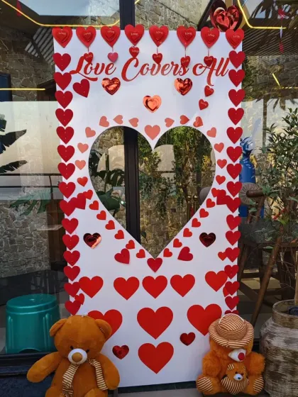 A fun and interactive photo booth frame for Valentine's Day. This cutout is decorated with red hearts and a "Love Covers All" message, complete with cute teddy bears.
