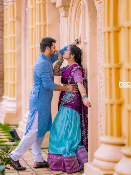 A playful and romantic moment between a couple in colorful traditional wear. The groom leans in for a kiss against a backdrop of golden pillars, creating a warm and happy scene.