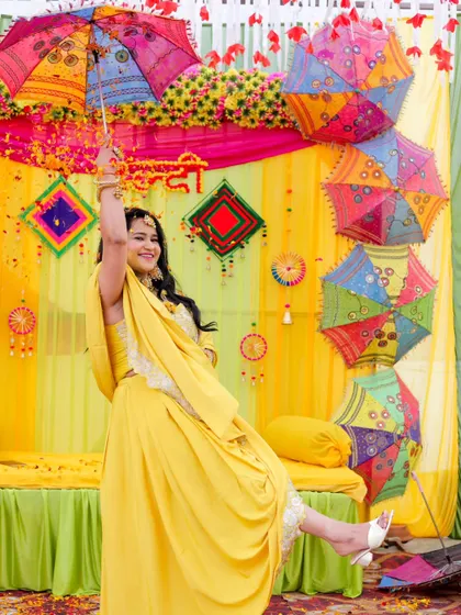 A playful bride at her Haldi ceremony, kicking up her leg and smiling under a colorful umbrella. This photo is full of personality and joy.