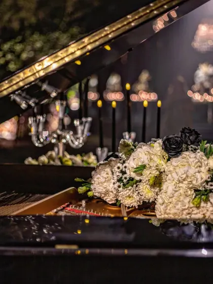 A close-up of a floral bouquet placed artfully on the grand piano. The contrast of the pure white hydrangeas and the rare black roses creates a visually arresting composition.