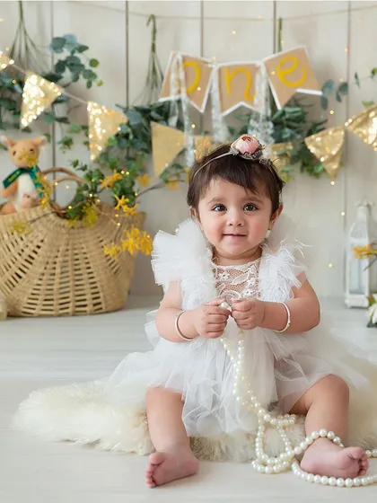 A gentle smile from a sweet baby girl during her milestone session. She is sitting on a soft rug, playing with pearls, in a lovely rustic setting.