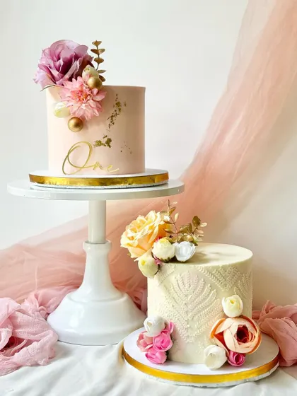 A duo of stunning floral cakes. One features a textured knit pattern, while the other is smooth with gold leaf, both adorned with beautiful silk flowers.