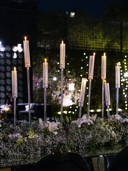 A beautiful tabletop centerpiece featuring tall, slender candles rising from a bed of white flowers, creating a romantic and ethereal glow.