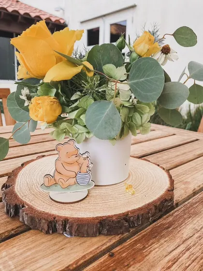 A Winnie the Pooh "Mommy Bee" baby shower. This centerpiece, featuring a Pooh Bear cutout on a wood slice, is a charming detail for the tables.