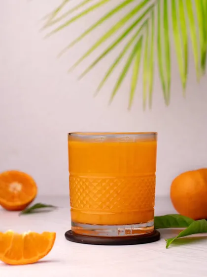 A bright and airy shot of a glass of fresh orange juice. The clean, minimalist styling with a palm leaf in the background gives it a healthy and refreshing vibe.