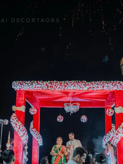 This is a striking red wedding mandap set up for an outdoor ceremony. The structure is covered in red fabric and decorated with red and white flowers, creating a vibrant look against the night sky.