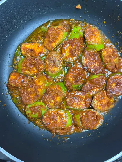 A top-down view of the raw banana roast cooking in the pan. The vibrant red of the chili paste against the green of the raw banana is a feast for the eyes.