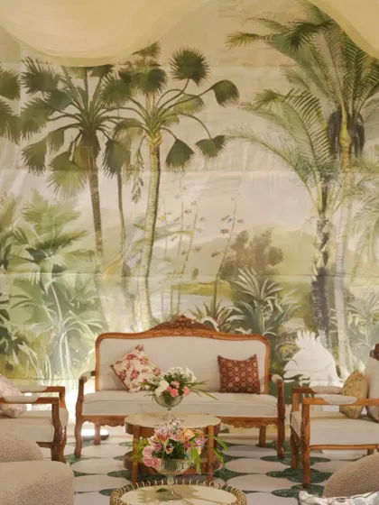 A serene Nikaah seating area. The vintage-style ivory sofa and chairs with intricate wooden frames are set against a lush, hand-illustrated palm backdrop, creating a timeless and intimate feel.
