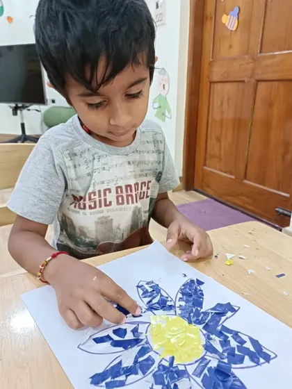 A young boy concentrates on his paper collage art, carefully placing each piece. We create a calm environment where children can focus on their work.