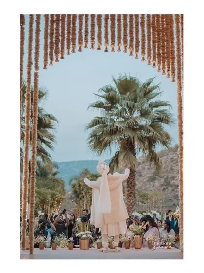 The groom's grand entrance, standing triumphantly at the mandap against a backdrop of palm trees and mountains.