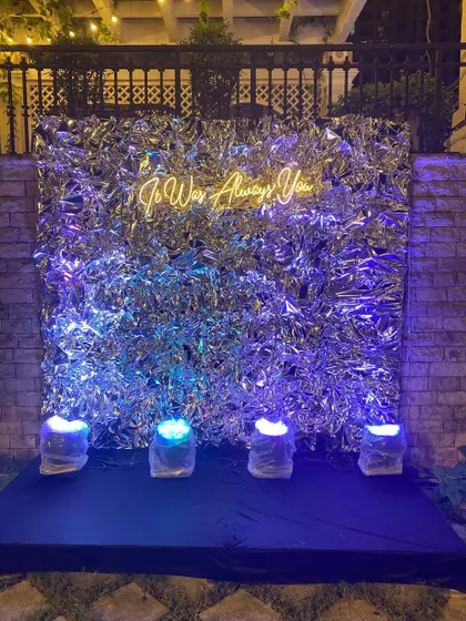 Your love story, lit up. We love creating modern, fun photo booths like this one, featuring a shimmering silver backdrop and a custom neon sign that reads 'It Was Always You' for a perfect sangeet night picture spot.