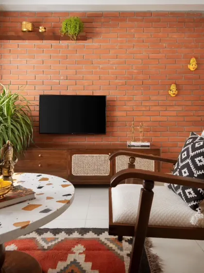 In the Reddy Home, an exposed brick feature wall serves as a warm, textured backdrop for the living area. This element, referencing mid-century modernism, contrasts with the neutral plaster walls and complements the custom teak and cane furniture.
