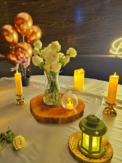 A close-up of a romantic table setting, with a floral centerpiece, candles, and rose gold balloons.