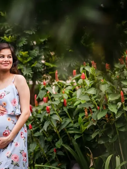 The maternal glow is real. This outdoor maternity portrait captures an expecting mother in a beautiful floral dress, surrounded by lush greenery and flowers. The natural setting complements the natural beauty of pregnancy.