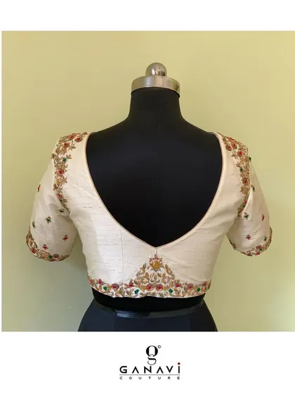 A classic V-neck blouse in raw silk, adorned with colorful floral embroidery along the neckline and sleeves. The open-back design adds a touch of modern sensibility to this beautifully crafted piece.