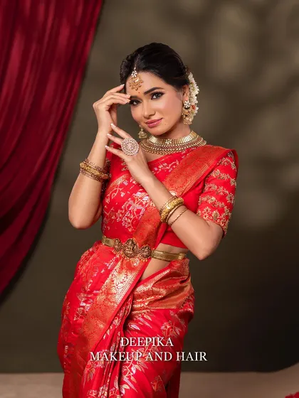 The bride strikes a pose, showcasing her beautiful red saree and the intricate gold embroidery on her blouse. The makeup is classic and timeless.