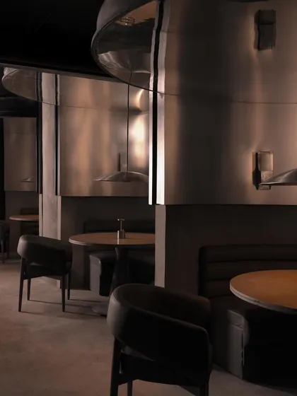 The main dining area of Lair, where curved metal partitions create semi-private booths. The reflective surfaces create a disorienting yet captivating play of light and shadow.