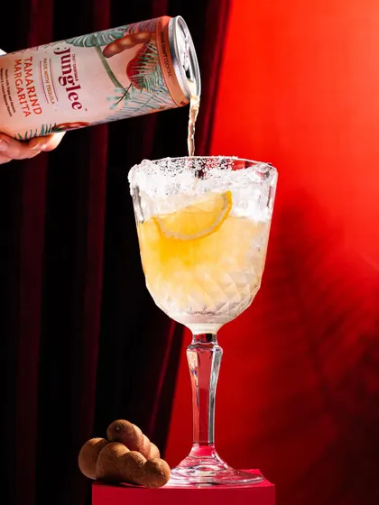 A canned tamarind margarita being poured into a salt-rimmed glass. This shot elevates a ready-to-drink product by showing it in a sophisticated serving style.