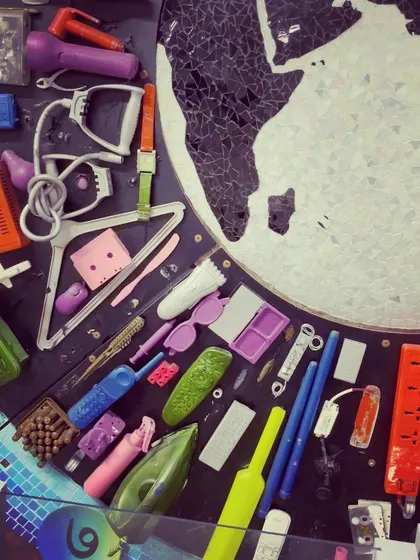 A close-up view reveals the individual items that make up the mural. You can spot things like old irons, remote controls, clothes hangers, and plastic toys, each with its own history.