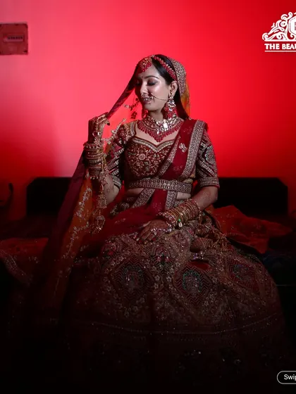 A dramatic, moody shot of a bride in a classic red lehenga. The lighting highlights the rich color of her outfit and the flawless finish of her makeup.