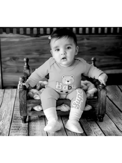 A black and white portrait of baby Navya, one of the six-month-old twins. The wooden backdrop and floor add rustic texture to this sweet and simple baby photo.