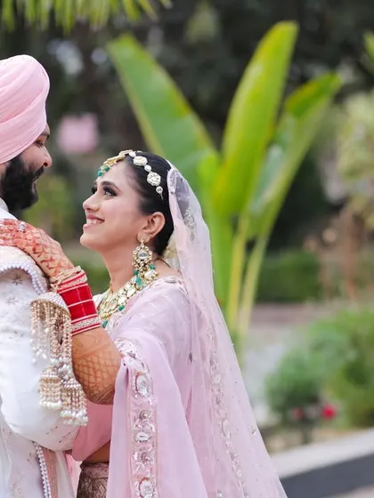 An intimate moment between a Sikh bride and groom, sharing a look of love. The photo highlights the bride's soft pink attire and traditional red chooda bangles.