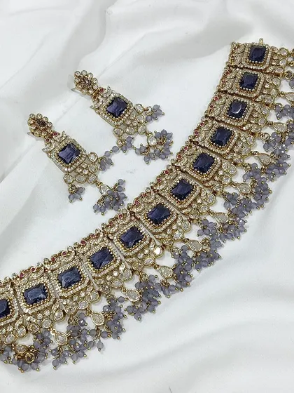 A popular choker design featuring square-cut stones, available in a variety of colors like emerald green, white, aqua blue, and baby pink. The matching earrings complete this elegant and modern ethnic set.