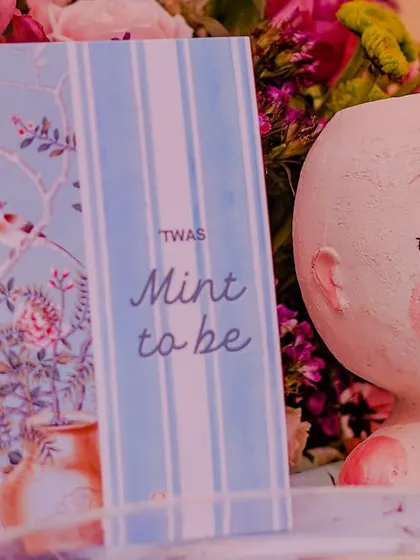A close-up of the 'Mint to be' themed card, placed next to a charming, face-shaped vase. These personalized details make the celebration feel truly special.