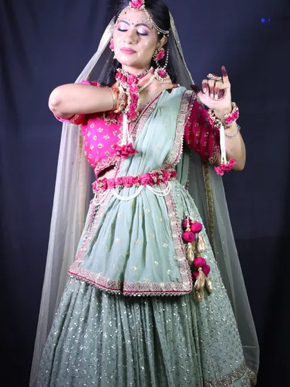 A client dressed for her Haldi or Mehendi ceremony in a mint green lehenga with a bright pink blouse, adorned with matching floral jewellery.