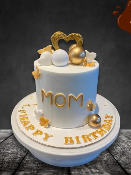 A classic and elegant birthday cake for Mom. The clean white fondant is accented with gold lettering, delicate hearts, and shimmering spheres, creating a sophisticated look for her special day.