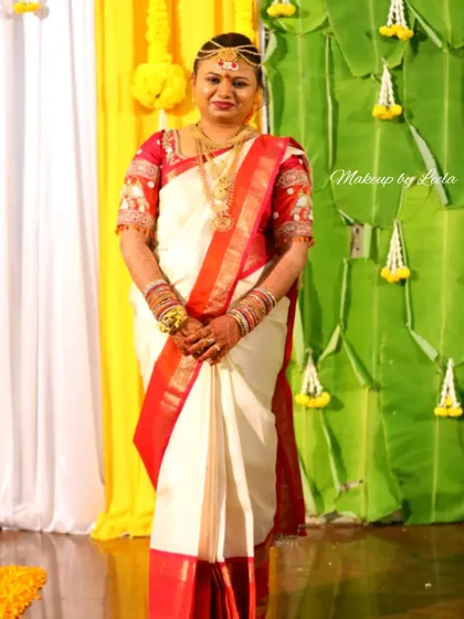 A bride in a classic white and red silk saree, a popular choice for Muhurtham ceremonies. The makeup is traditional, with a prominent bindi and gold jewelry.
