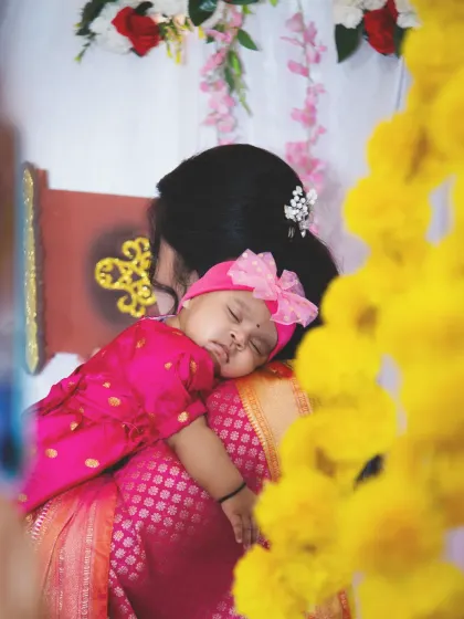 A precious, candid shot from a naming ceremony, showing a newborn baby sleeping peacefully on her mother's shoulder.