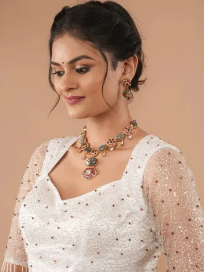 A model wears a sparkling white blouse with a unique stone necklace, demonstrating a chic and contemporary party look.