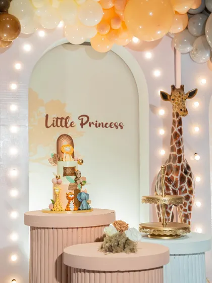 A "Little Princess" safari cake setup. This unique theme combines the wildness of the jungle with the sweetness of a princess party, featuring a giraffe and a themed cake.