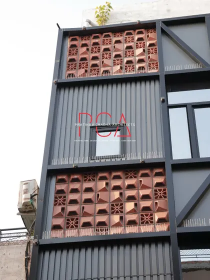 A close-up of the facade, detailing the pattern of the terracotta jaalis and their integration with the metal framework and louvers.