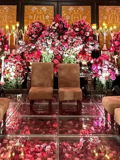A view of the seating on the glass floor stage, surrounded by a profusion of red flowers. This design offers a unique and immersive experience for the couple and their families.