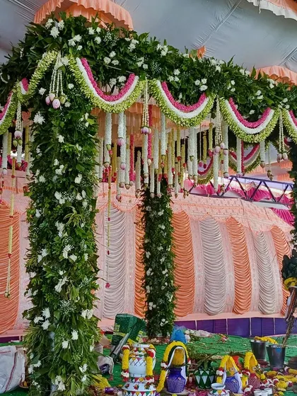 A close-up of the intricate floral work on a traditional mandap, combining green leaves with pink and white flowers.