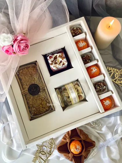 An open view of a signature Diwali hamper, featuring a coffee walnut tea cake, nutty truffles, and motichoor ladoo-inspired candles.