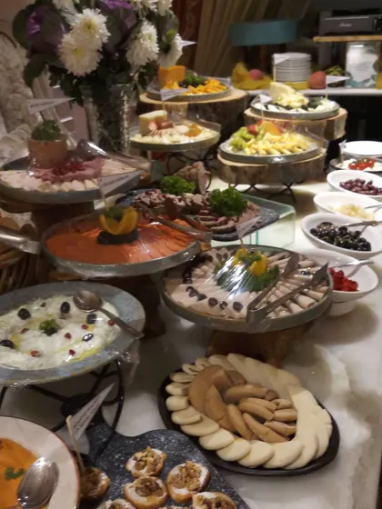 A multi-tiered buffet display with a variety of Mediterranean and international dishes. Using wooden logs and slate platters for presentation adds a rustic yet sophisticated touch to this house party setup.