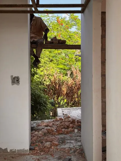 A worker sits on a scaffold plank inside an unfinished room at Kizikula. The simple opening provides a framed view of the lush greenery outside, a key element of the design.