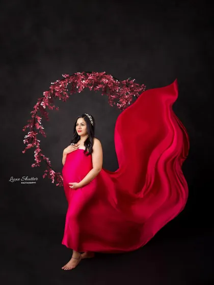 A beautiful composition featuring a floral hoop behind the mom-to-be, whose red gown and flowing fabric create a stunning visual.