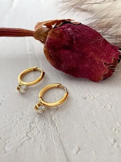 An artistic shot of my small hoop earrings with sparkling crystal charms, placed next to a dried rose. These are delicate, romantic, and made from color-stable stainless steel.