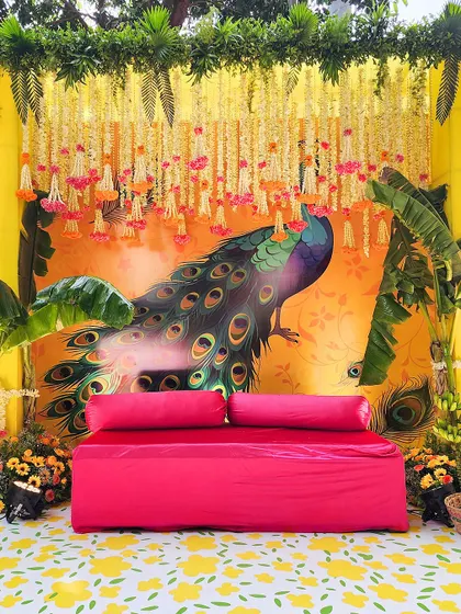 Our thematic decor brings stories to life. This vibrant Mehendi seating features a beautiful hand-painted peacock backdrop, a fuschia sofa, and traditional floral strings for a festive feel.