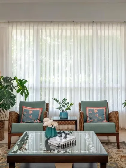 The finished living room in 'House of Kismish', filled with light from the large windows, comfortable seating, and lush indoor plants, creating a serene and formal gathering space.