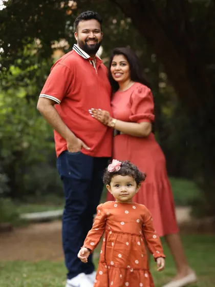 A classic family standing portrait in the park. The little girl takes center stage, showcasing her personality while her parents stand lovingly behind her.