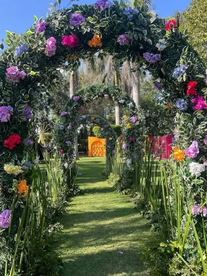 A magical garden walkway created with a series of arches covered in lush greenery and colorful flowers, perfect for a fairytale-themed Mehendi.